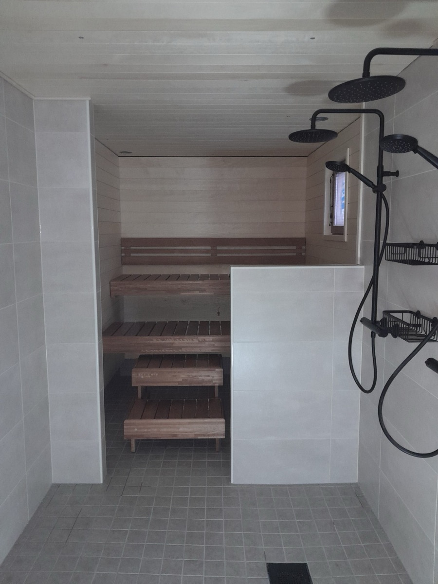 Sauna ja suihkutila: puulauteet lasiseinän takana, mustat suihkukalusteet ja laattalattia