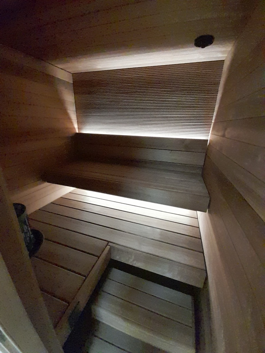 Saunan lauteet epäsuoralla valaistuksella ja rimoitettu selkänojaseinä