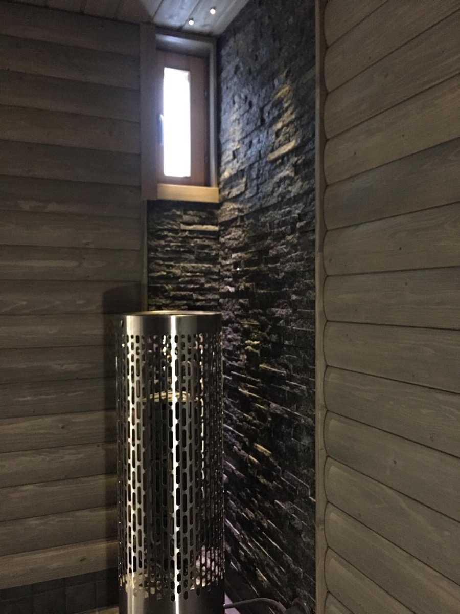 Sauna: tumma kiviseinä kiukaan takana ja harmaaksi käsitelty puupaneeli